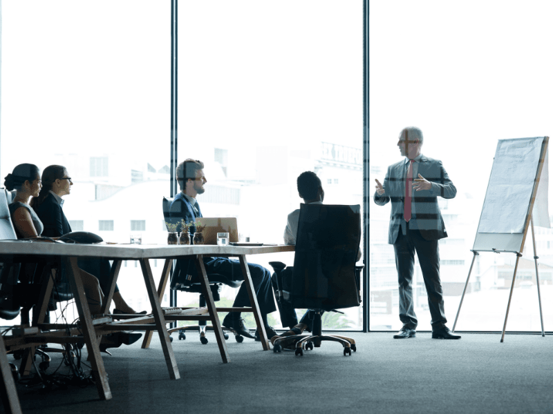Advisor briefing a seated team in a glass-walled meeting room