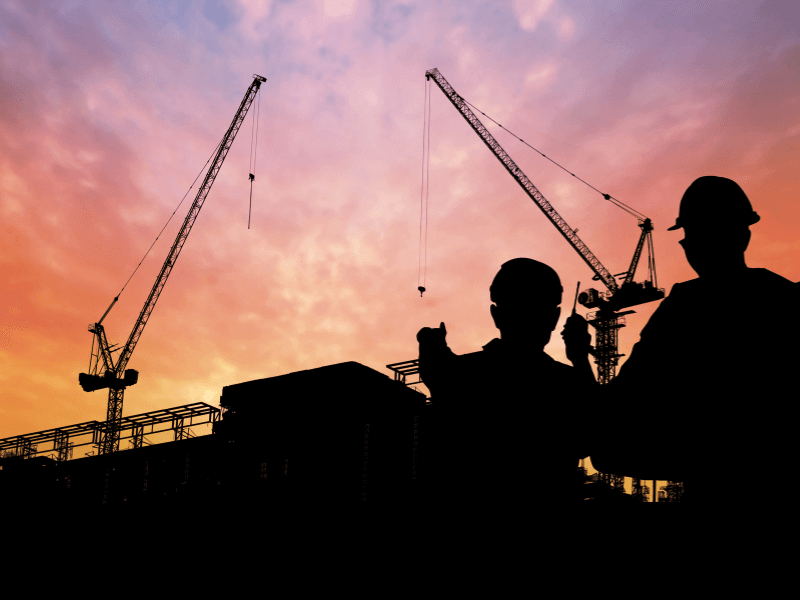 Silhouetted site crew and tower cranes against a dusk sky