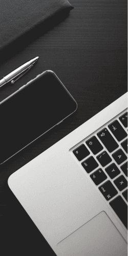 Laptop, phone and notebook arranged on a dark desk