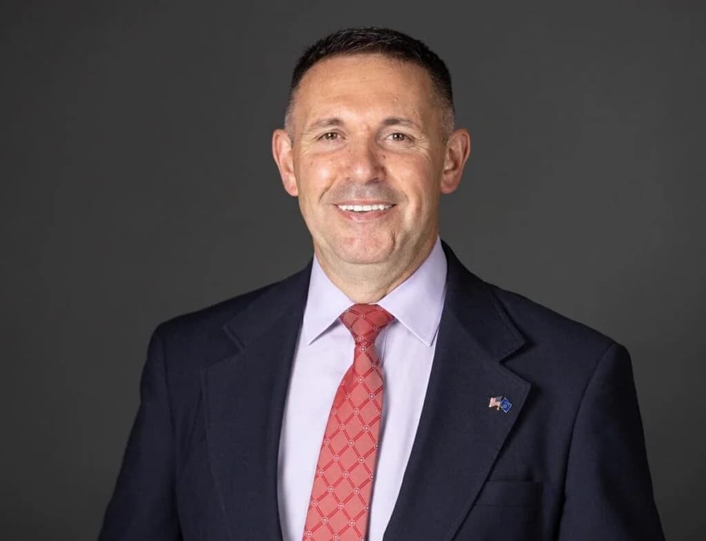 Portrait of Xhavit Gashi in a navy suit against a grey background